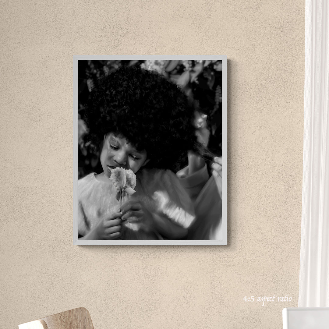 Black and white photo of a child holding flowers in a frame on a beige wall.