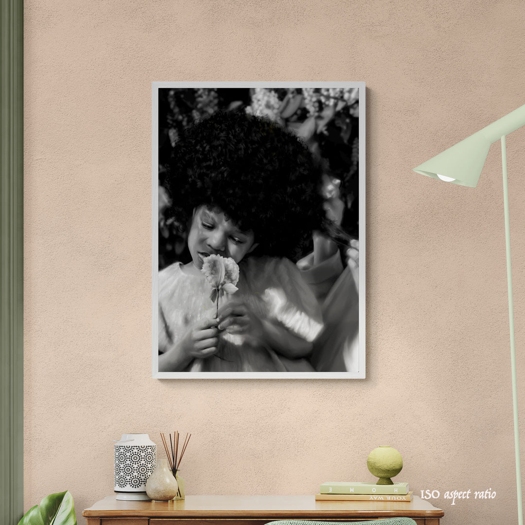 Framed black and white photo of a child holding a flower on a wall with a lamp and decor items below.