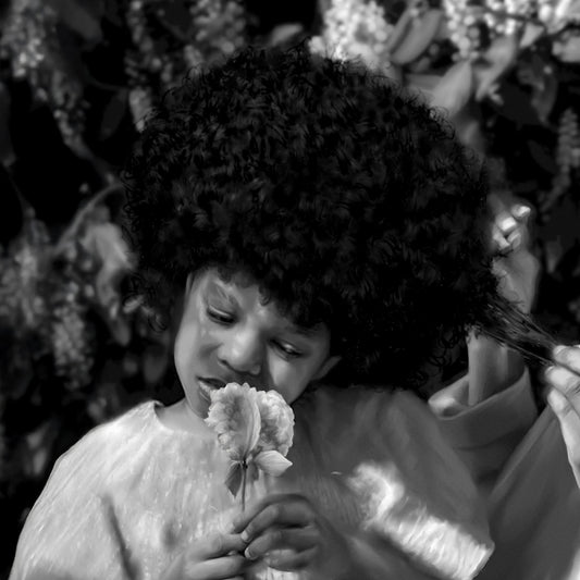 Black and white photo of a child smelling a flower outdoors